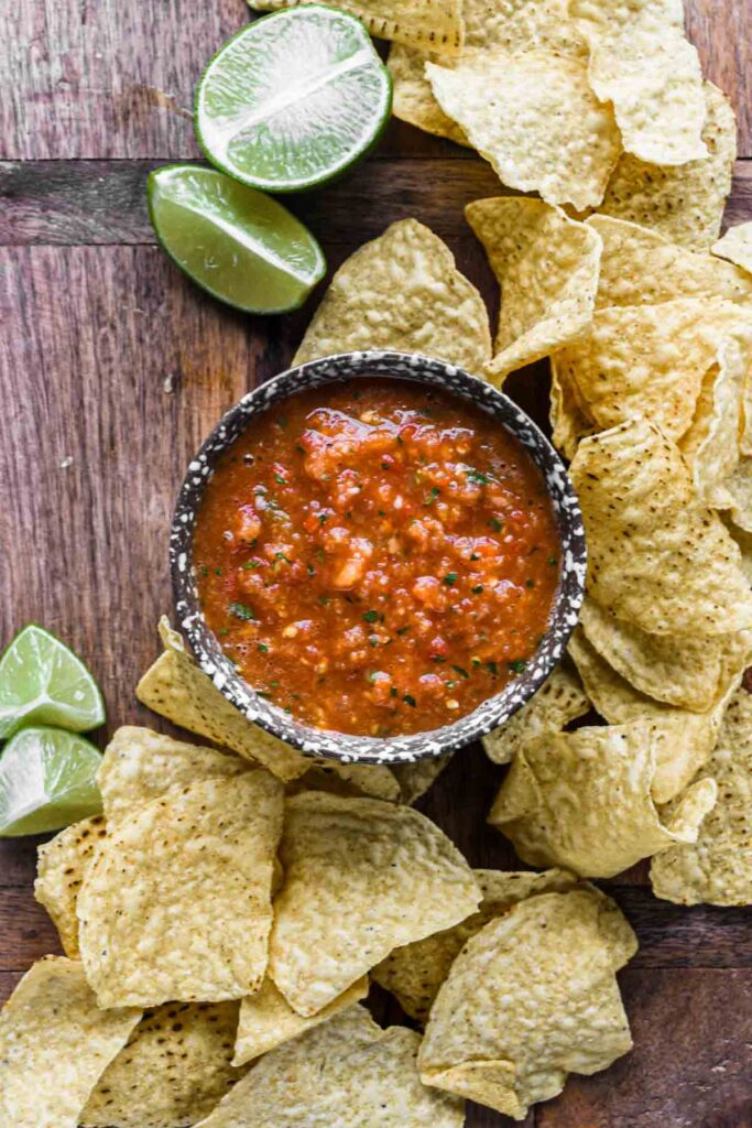 Salsa on a wood board surrounded by chips and limes.
