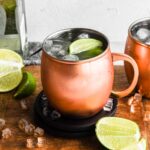 Shot of the finished tequila mule in a copper mug surrounded by ice and limes.