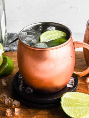 Shot of the finished tequila mule in a copper mug surrounded by ice and limes.