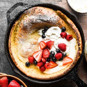 Close up image of the finished dutch baby with whipped cream and berries.