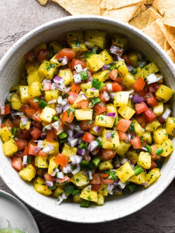 A bowl of pineapple pico de gallo with chips and limes.