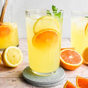 Orange lemonade in a glass on a blue coaster.