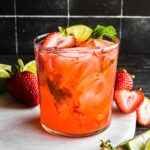 Strawberry mint margarita in a glass topped with a strawberry slice, lime, and mint.