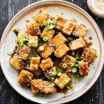 Finished honey garlic tofu dish on a plate with green onions and sesame seeds.