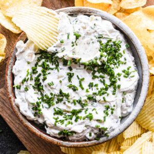 Sour cream and onion dip in a bowl with a ruffled chip dipped in.