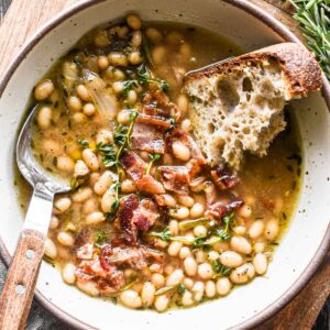 Close up image of brothy beans in a bowl topped with bacon.