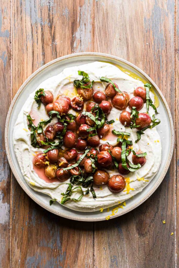 Whipped goat cheese on a plate with roasted grapes and basil on top.