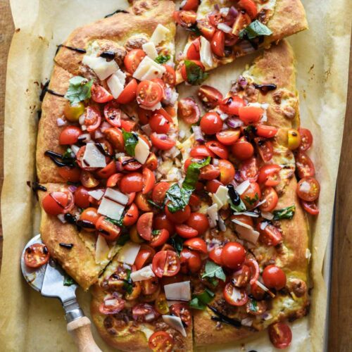 Finished pizza topped with bruschetta, balsamic glaze and shaved parmesan cheese.