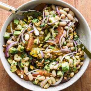 white bean citrus salad in a serving bowl with two serving spoons.