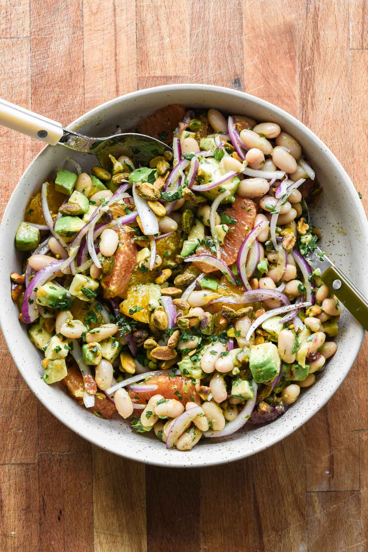 white bean citrus salad in a serving bowl with two serving spoons.