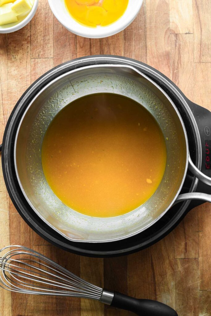 Passion fruit and sugar melting in a stainless steel pot.