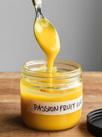 Passion fruit curd in a labeled jar with a spoon dipping.