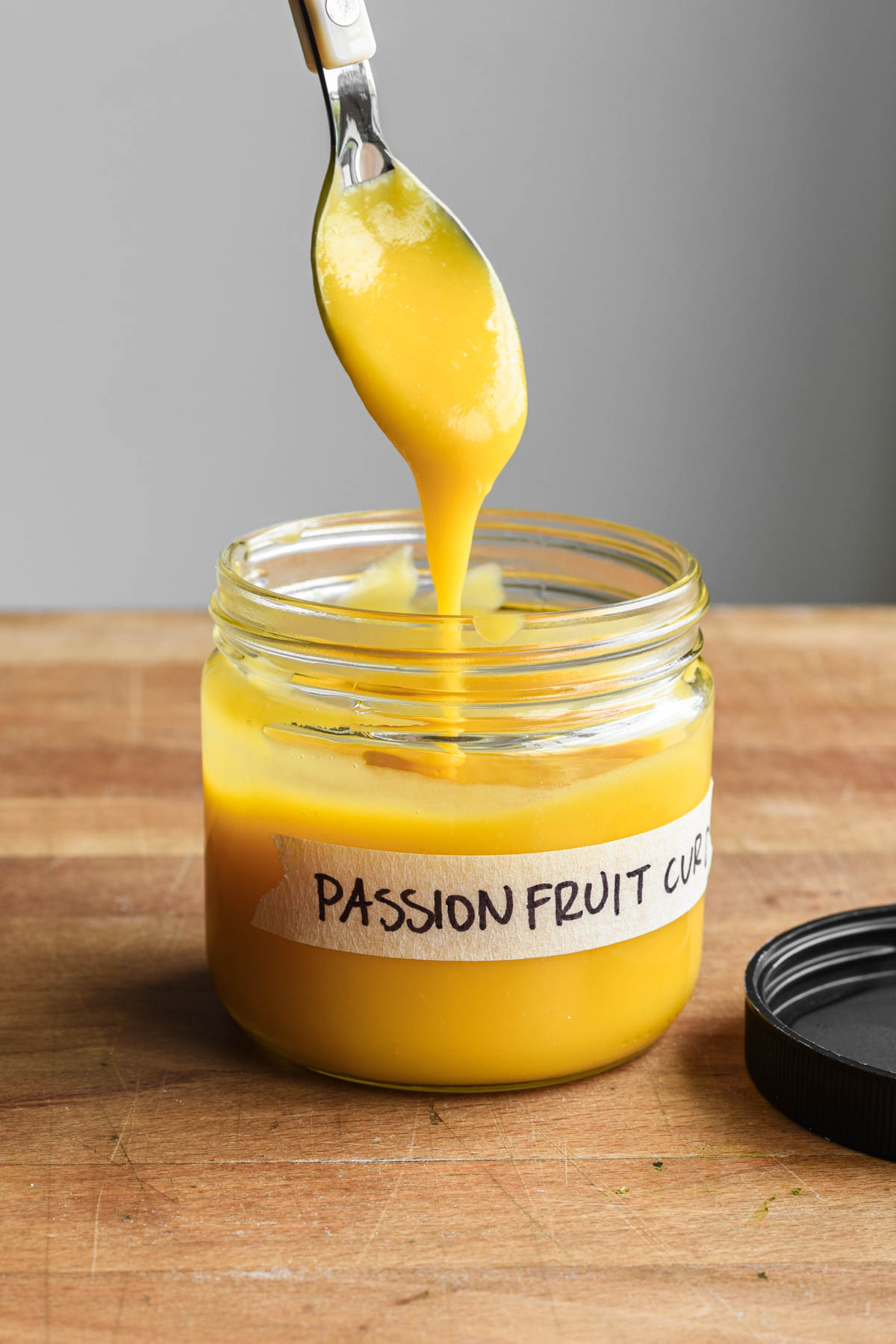 Passion fruit curd in a labeled jar with a spoon dipping.