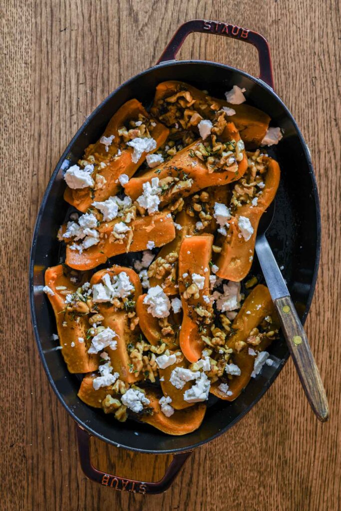 Roasted honeynut squash in a red staub baking dish.